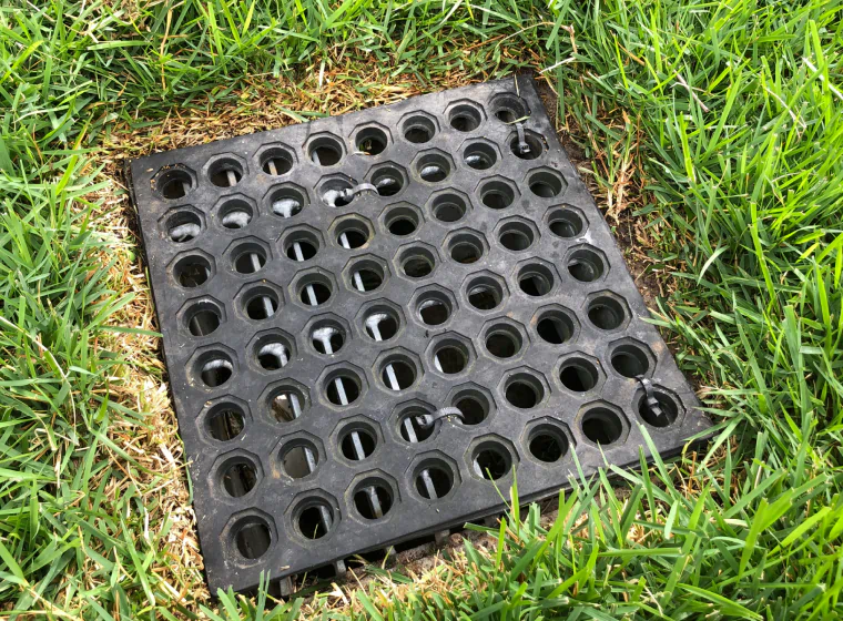 french drain with a black cover on the middle of a space in the ground with grass around