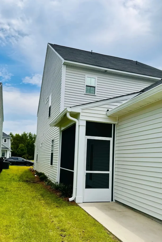 Two-story home with light siding, white gutters and downspout, and a screened-in porch along the side, with neighboring houses visible in the background.