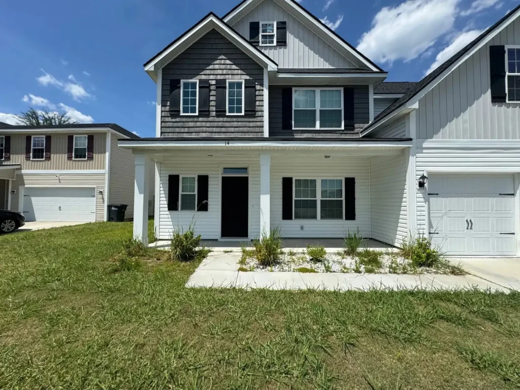 Two-story home with gray and white siding, black shutters, a covered front porch, and white gutters, set on a grassy lot in a residential neighborhood.