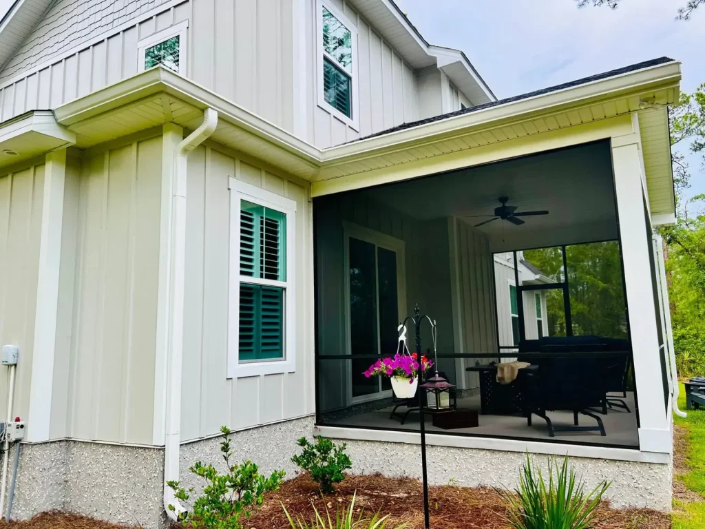 Home exterior with light vertical siding, white gutters and downspout, and a screened-in patio with outdoor seating and hanging plants.