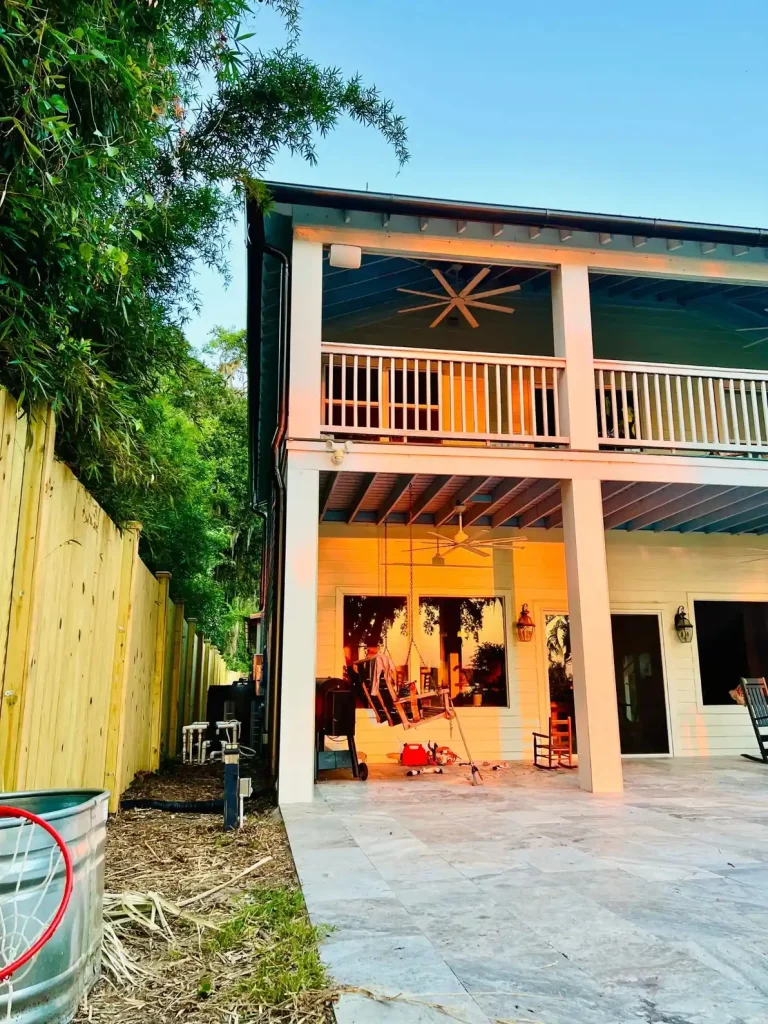 Two-story home with upper and lower covered decks, white gutters, and ceiling fans, overlooking a fenced backyard with outdoor seating.