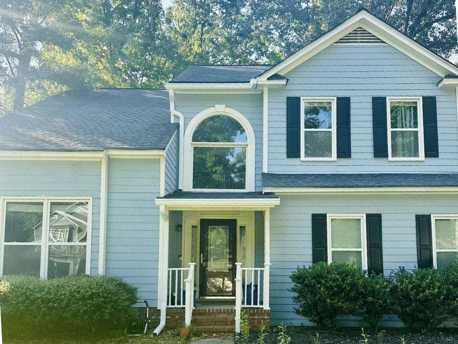 Two-story home with blue siding, white trim, black shutters, and white gutters, featuring an arched window above the front entry and surrounded by trees and shrubs.