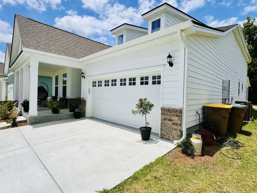Front view of a white house garage with a double door, decorative windows, black exterior lights, and visible gutters and downspout under a partly cloudy sky.